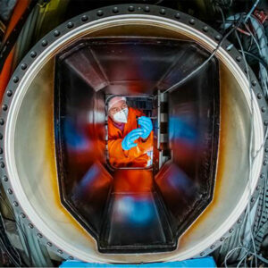 A view through a port looking into the vessel shows an operations team member working on DIII-D